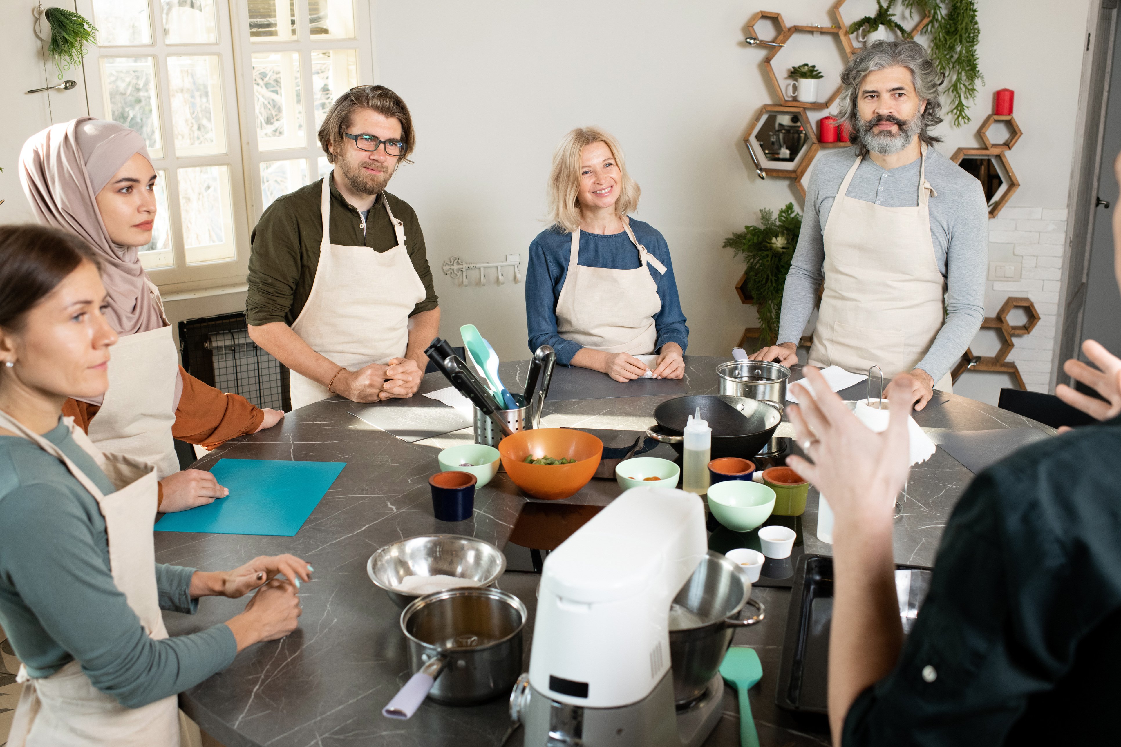 Group-of-young-and-mature-people-in-aprons-looking-at-male-cooking-coach-and-listening-to-him-1309278213_3868x2578